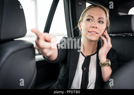 Businesswoman on call pointing finger in car  Stock Photo