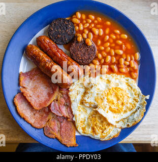 overhead view of a full english fried breakfast of eggs bacon beans and sausages on a café table. Stock Photo