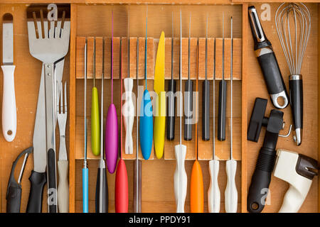 Fitted knife drawer in a wooden kitchen cabinet with a neat array of knives with assorted cooking utensils in a full frame overhead view Stock Photo