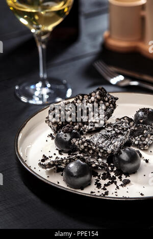 Appetizer with salmon pate, ink cuttlefish, crackers served on white tray over black wooden background. Close-up. Photo for the menu. Molecular gastro Stock Photo