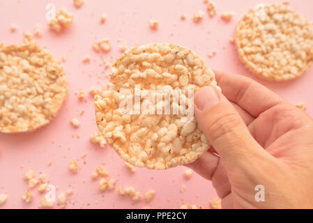Rice cakes in male hand over pastel pink background, overhead view Stock Photo