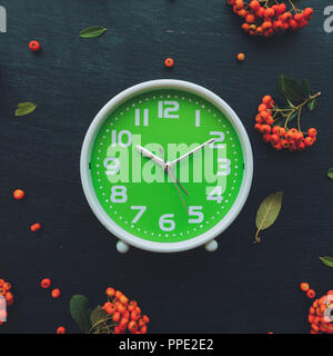 Plastic green alarm clock on dark wooden background, flat lay top view minimal composition with retro wild berry fruit arrangement Stock Photo