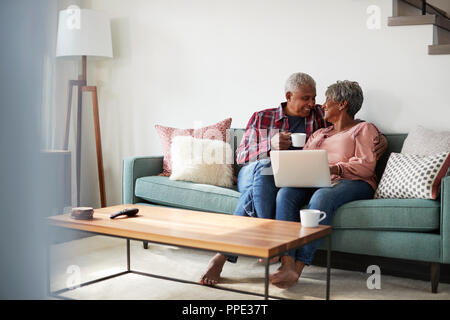 Senior Couple Sitting On Sofa At Home Using Laptop To Shop Online Stock Photo