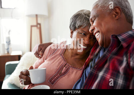 Loving Senior Couple Sitting On Sofa At Home Relaxing With Hot Drink Stock Photo