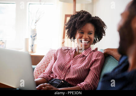 Couple Sitting On Sofa At Home With Woman Using Laptop Computer Stock Photo