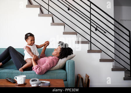 Mother Lying On Sofa At Home Playing With Baby Daughter Stock Photo