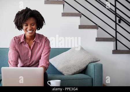 Woman Sitting On Sofa At Home Using Laptop Computer Stock Photo