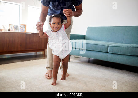 Father Encouraging Baby Daughter To Take First Steps At Home Stock Photo
