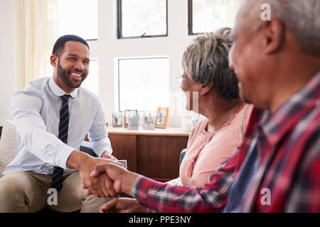Senior Couple Shaking Hands With Male Financial Advisor At Home Stock Photo
