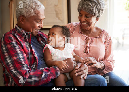 Grandparents Sitting On Sofa With Baby Granddaughter At Home Stock Photo
