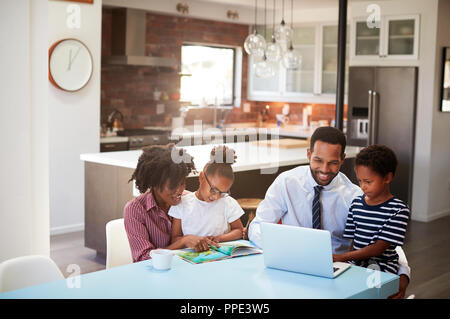 Parents Sitting Around Table At Home Helping Children With Homework Stock Photo