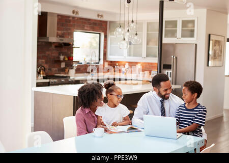 Parents Sitting Around Table At Home Helping Children With Homework Stock Photo