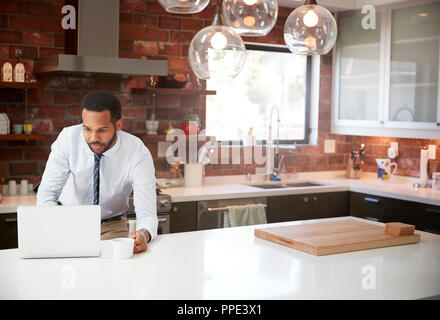 Businessman Using Laptop On Kitchen Island Before Leaving For Work Stock Photo