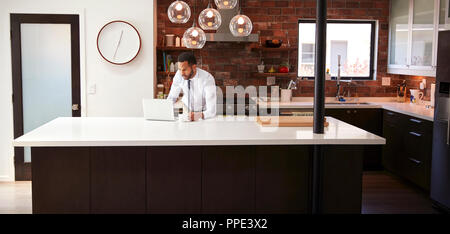 Businessman Using Laptop On Kitchen Island Before Leaving For Work Stock Photo