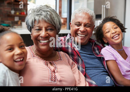 Portrait Of Grandparents Sitting On Sofa At Home With Granddaughters Stock Photo