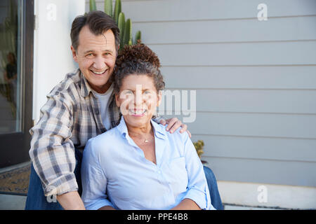 Portrait Of Senior Couple Sitting Outside Grey Clapboard House Stock Photo
