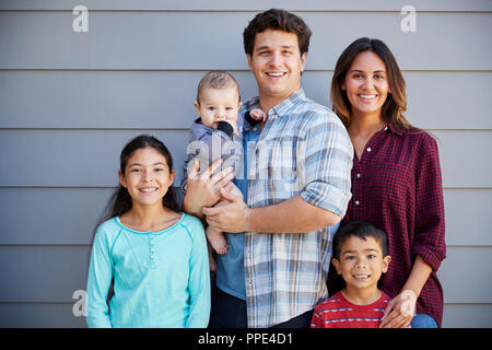 Portrait Of Happy Family With Baby Standing Outside Grey Clapboard House Stock Photo