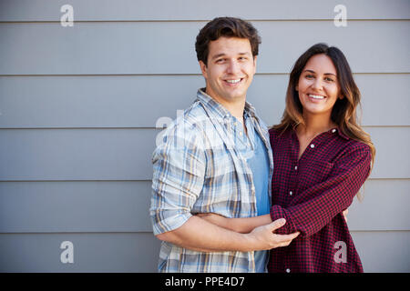 Portrait Of Couple Standing Outside Grey Clapboard House Stock Photo