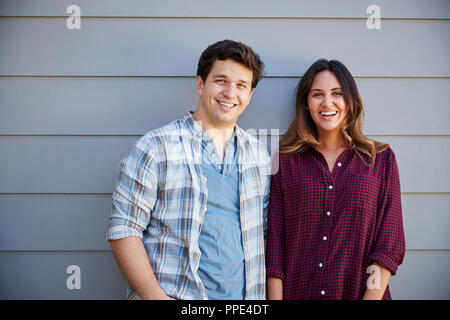 Portrait Of Couple Standing Outside Grey Clapboard House Stock Photo