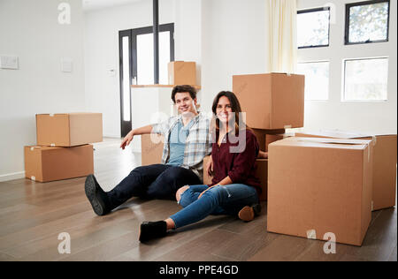 Portrait Of Happy Couple Sitting On Floor Surrounded By Boxes In New Home On Moving Day Stock Photo