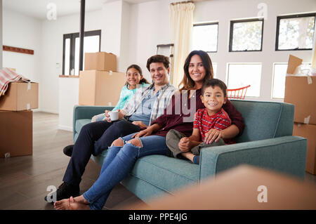 Portrait Of Happy Family Resting On Sofa Surrounded By Boxes In New Home On Moving Day Stock Photo