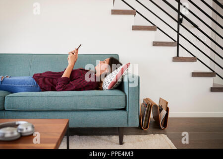 Side View Of Woman Lying On Sofa At Home Using Mobile Phone Stock Photo