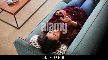 Overhead View Of Woman Lying On Sofa At Home Using Mobile Phone Stock Photo