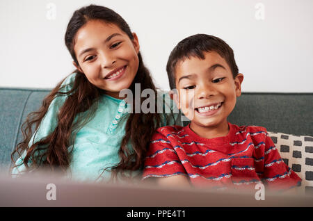 Brother And Sister Sitting On Sofa At Home Having Fun Playing On Laptop Together Stock Photo