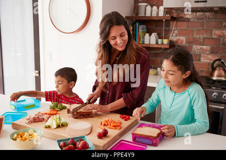 Children Helping Mother To Make School Lunches In Kitchen At Home Stock Photo