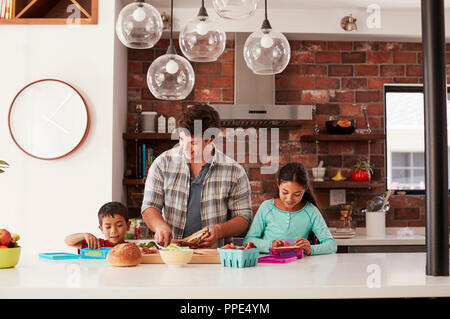 Children Helping Father To Make School Lunches In Kitchen At Home Stock Photo