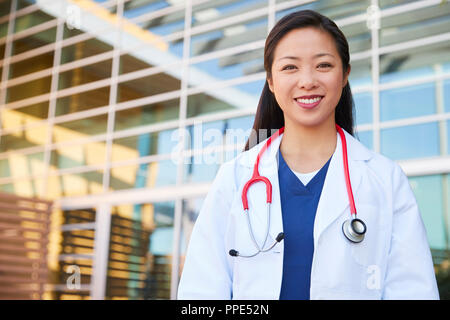 Smiling Asian female healthcare worker outdoors in lab coat Stock Photo