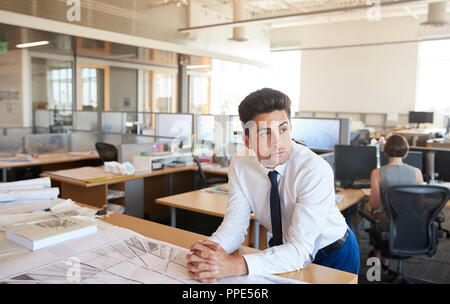 Young male architect leaning on desk in open plan office Stock Photo