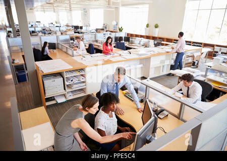 Colleagues working at a woman’s workstation in a busy office Stock Photo