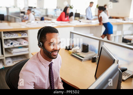 Smiling black male call centre worker looking at screen Stock Photo