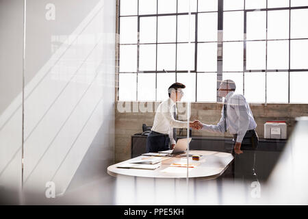 Two businessmen seen through window shaking hands in office Stock Photo