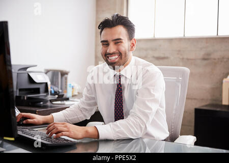 Young Hispanic businessman using computer smiling to camera Stock Photo