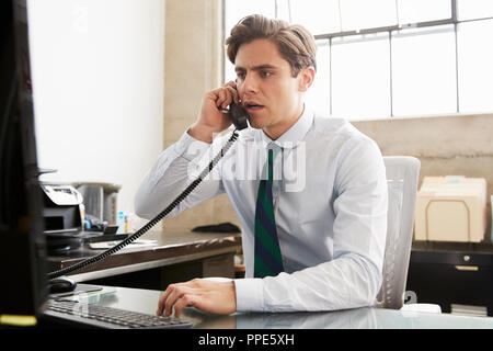 Young white businessman on the phone at an office desk Stock Photo