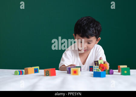 3 years old Asian boy play toy or square block puzzle on green chalkboard or school board background, kid lying learn by playing block shape or pieces Stock Photo