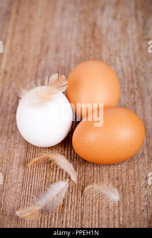 three eggs and feathers on rustic wooden table Stock Photo