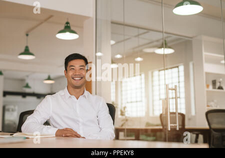 Successful Asian businessman smiling while sitting at his office desk Stock Photo