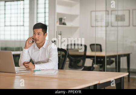 Young Asian businessman talking on his cellphone in an office Stock Photo