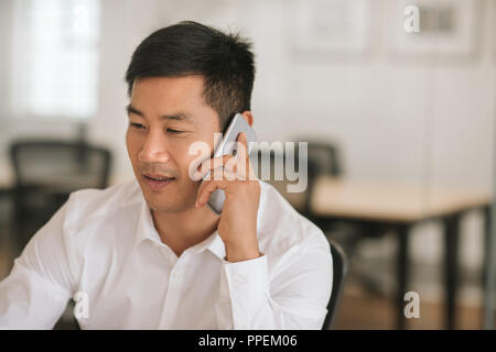 Smiling Asian businessman talking on a cellphone at work Stock Photo