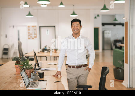 Smiling Asian businessman standing by his desk in an office Stock Photo