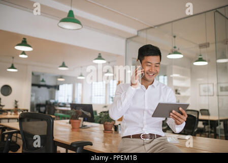 Asian businessman talking on his cellphone and holding a tablet Stock Photo