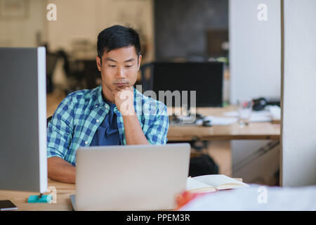 Asian designer sitting at his office desk focused on work  Stock Photo