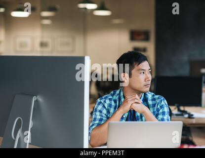 Young Asian designer sitting at his desk thinking about work  Stock Photo