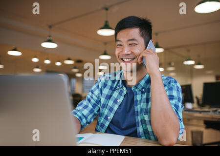 Smiling Asian designer talking on a cellphone in an office  Stock Photo