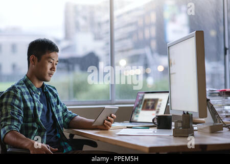 Young Asian designer using a tablet at his desk Stock Photo