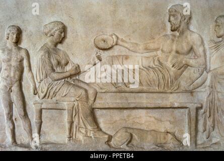 Greek art. Classical period. Grave stele. Relief. Funerary banquet scene. The man lying holding in his hand a 'Philae' and a boy came from a crater serves. Dated in 400 BC, was found in the Asklepieion (Piraeus). National Archaeological Museum. Athens. Greece. Stock Photo