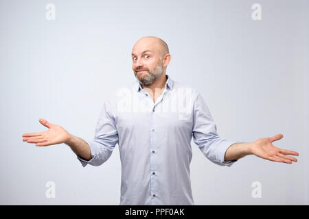 Confused mature bearded man standing and shrugging shoulders isolated over white background. Stock Photo